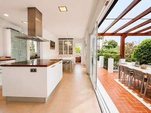 Een moderne keuken met een centraal eiland, een eethoek met uitzicht op een terras, en een grote glazen deur die leidt naar buiten.