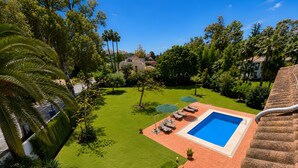 A swimming pool with a tiled deck, surrounded by a well-manicured lawn and various trees. - Villa 'Gran Cerca De Puerto Banús' with Mountain Views, Wi-Fi, and Air Conditioning (Marbella)