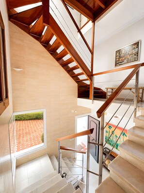 Een modern interieur met een trap, uitzicht op een betegeld terras en een schilderij aan de muur.