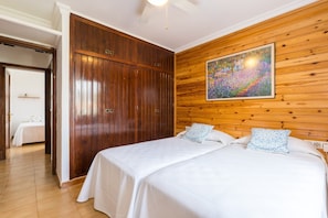 A bedroom with a wooden headboard, a large painting, and a double bed with patterned pillows. - Wonderful Holiday Home 5ª Avenida (S'Algar)