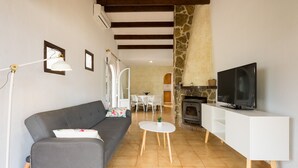 Uma sala de estar com sofá, televisão, armário branco, lareira de pedra e um espaço para refeições.