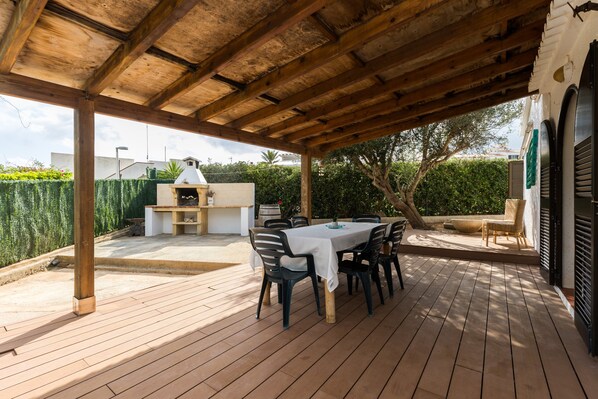 An outdoor patio with a wooden table and chairs, a barbecue grill, and a covered seating area.