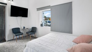 Een slaapkamer met een bed, twee stoelen, een televisie en een raam met uitzicht op auto's.