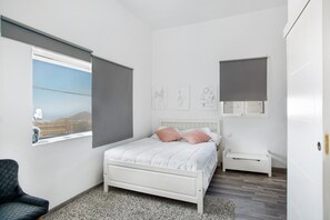 Une chambre à coucher avec un lit, une chaise, une fenêtre et des œuvres d’art accrochées au mur.