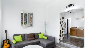 Een woonkamer met een grijze modulaire bank, een witte salontafel, een gitaar en uitzicht op de keuken door een boogvormige doorgang.