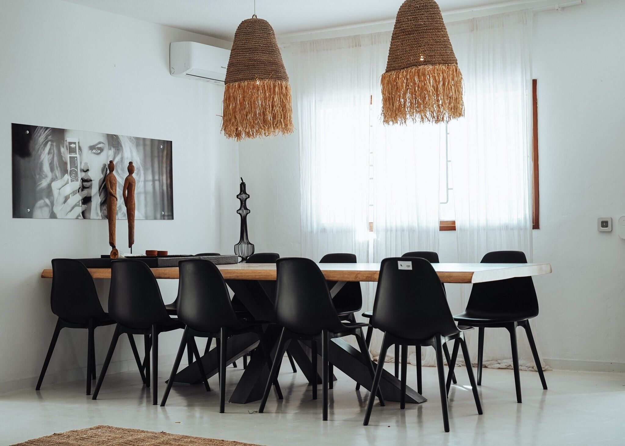 A modern dining area with a wooden table, black chairs, and two hanging woven light fixtures.