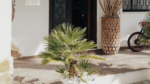 Entrada de Villa Shirla, con una puerta oscura, un muro blanco, una lámpara de macramé colgante y una planta alta en maceta.