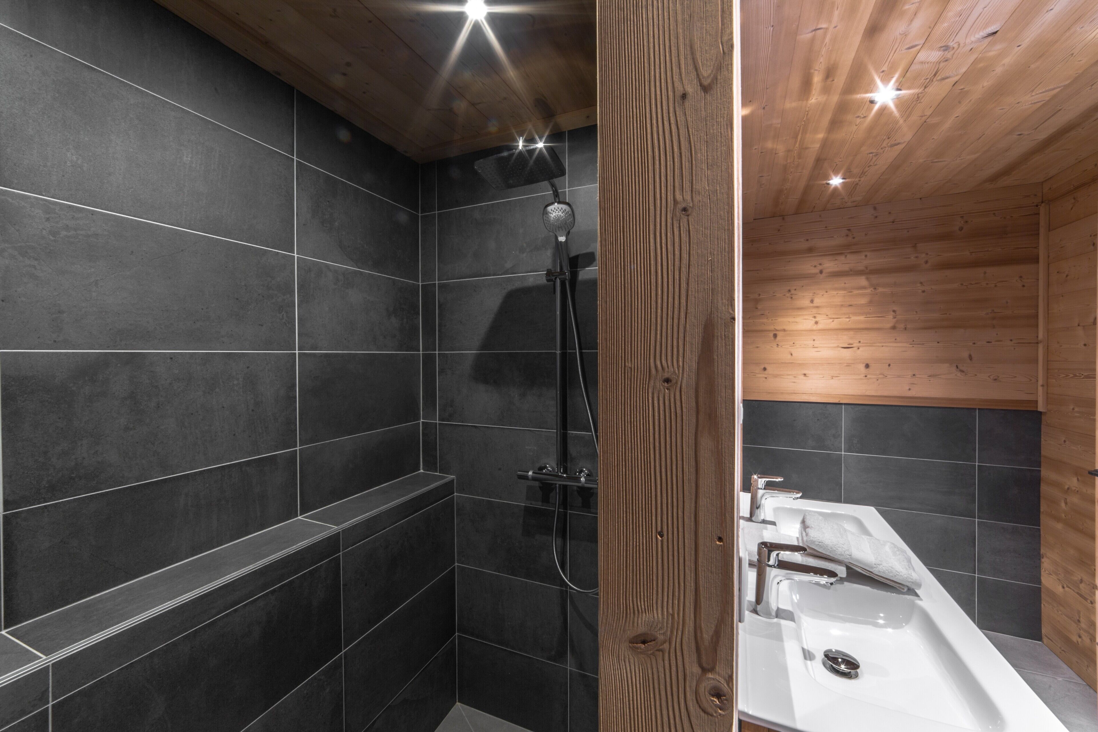 A modern bathroom with dark tiles, a shower, and a sink.