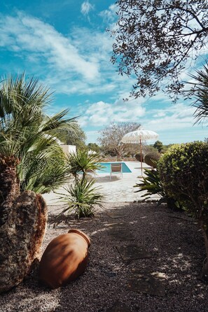 A garden area with a pool, palm trees, and a large umbrella.