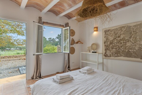A bedroom with a large bed, a window with curtains, a hanging basket, and a wall with decorative items.