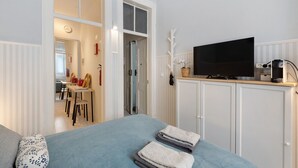 Une chambre à coucher avec un lit, un téléviseur posé sur un meuble, et une salle de bain visible à travers une porte ouverte.