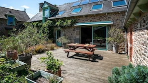 A stone building with a wooden deck, a picnic table, and potted plants. - Holiday Home 3 min from Beach – Private Terrace, Fenced Garden, Sleeps 5 (Plouha)