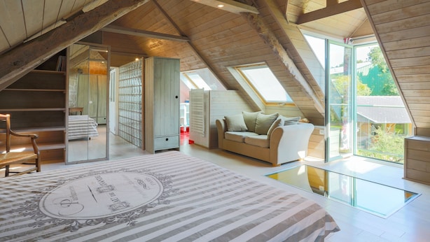 A spacious attic bedroom with a large bed, a sofa, and a glass floor leading to an outdoor area. - Holiday Home 3 min from Beach – Private Terrace, Fenced Garden, Sleeps 5 (Plouha)