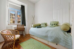 A bedroom with a bed, a chair, a window with curtains, and a view of buildings outside.
