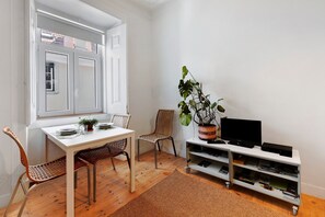 A room with a dining table, chairs, a TV on a stand, a bookshelf, and a potted plant.