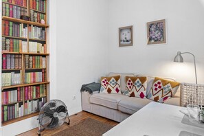 A room with a bookshelf, a sofa, a fan, and a table with a glass.