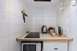 A compact kitchen with a microwave, kettle, and coffee maker on the counter, and a Zanussi refrigerator below.
