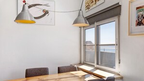 A dining area with a wooden table, four chairs, two pendant lights, a window with a view, and artwork on the walls.
