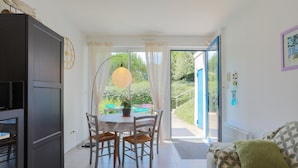 Une pièce comprenant une table à manger, des chaises, un canapé, un meuble et une porte vitrée donnant sur un espace extérieur.