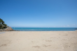 Una playa con cielos despejados, mar tranquilo y vegetación escasa.