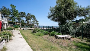 Un chemin menant à un bâtiment doté d’une terrasse, entouré de verdure et d’une clôture.