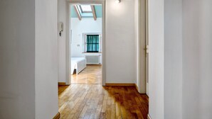 A hallway with wooden flooring, a skylight, and a view into a room with a radiator and a window with curtains.