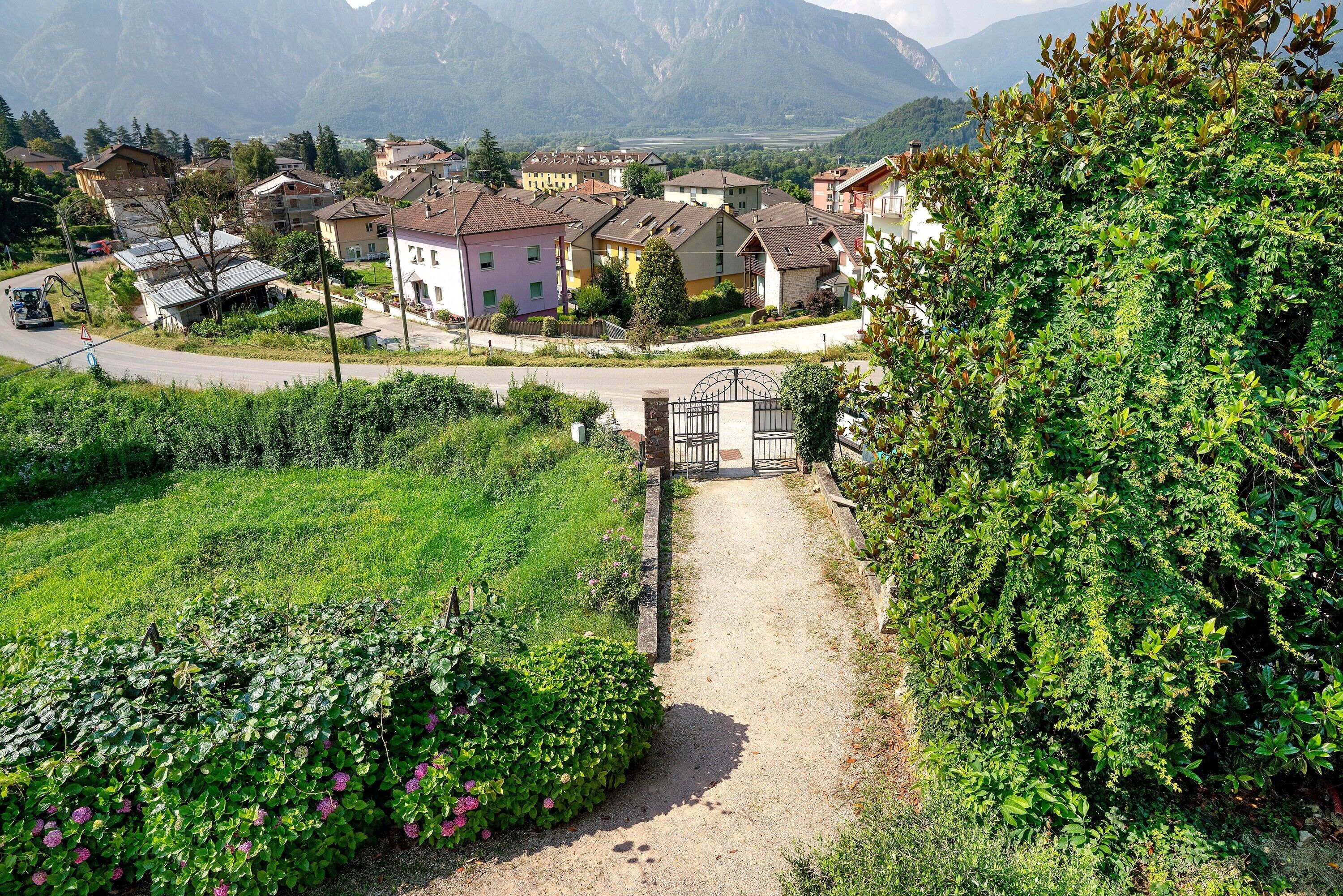 Un quartier résidentiel avec des maisons, une route asphaltée et un portail donnant accès à un sentier.