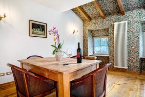 Uma sala de jantar com mesa de madeira, cadeiras de vime, uma garrafa de vinho e um vaso com flores.