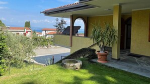 Een huis met een overdekte veranda, uitzicht op zee en een verzorgde tuin.