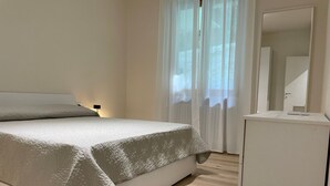 Een slaapkamer met een bed, nachtkastje, spiegel en een raam met gordijnen.