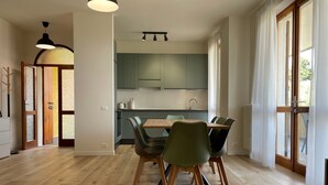 Een moderne keuken met groene kastjes, een eettafel met stoelen en een groot raam met gordijnen.