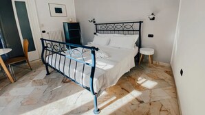 Ein Schlafzimmer mit einem Metallbett, einem kleinen Nachttisch, einem Sessel und einer Heizung.