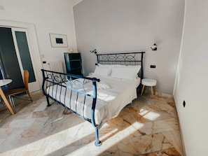 A bedroom with a metal-framed bed, a small bedside table, a chair, and a radiator.
