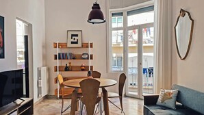 Ein Wohnzimmer mit rundem Tisch, Stühlen, einer Couch, einem Fernseher, einem Bücherregal und einem großen Fenster.