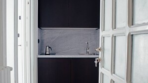 Eine schmale Küche mit dunklen Schränken, einer Arbeitsplatte, einem Wasserkocher und einem Wasserhahn.