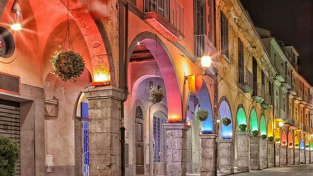 Eine Reihe von Gebäuden mit Rundbogenfenstern und steinernen Säulen, beleuchtet durch farbige Lichter.