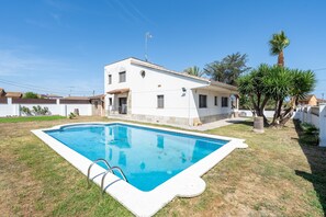 Uma casa de dois andares com piscina, uma palmeira e céu azul límpido.