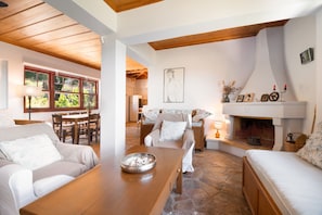 Un salon chaleureux avec une cheminée, un sol en pierre et un coin repas doté de meubles en bois.