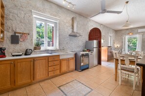 Una cocina con armarios de madera, un refrigerador de acero inoxidable, una estufa y un comedor con una mesa y sillas de madera.