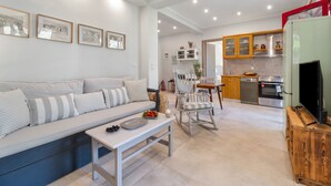 Una sala de estar moderna con sofá, mesa de comedor y zona de cocina con armarios y electrodomésticos.