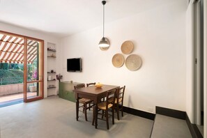 Un espace repas comprenant une table, des chaises, un luminaire suspendu, un téléviseur à écran plat et des éléments de décoration murale en fibres tressées.