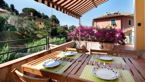 An outdoor dining area with wooden tables and chairs, a pergola overhead, and a view of surrounding buildings and greenery. - 'Terrazza Sivori' Apartment with Mountain View, Wi-Fi and Air Conditioning (bonassola)