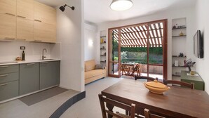A modern kitchen with built-in cabinets, a dining area with a wooden table and chairs, and a view through a glass door to an outdoor patio. - 'Terrazza Sivori' Apartment with Mountain View, Wi-Fi and Air Conditioning (bonassola)