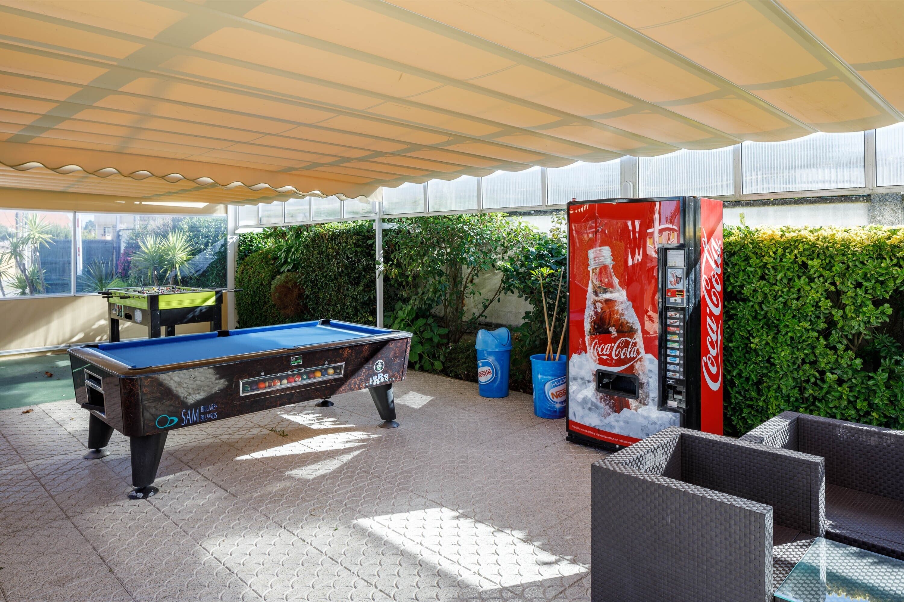 A pool table, outdoor seating, and a Coca-Cola vending machine in a covered outdoor area.