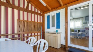 Un espace extérieur abrité, aménagé pour les repas, avec une table et des chaises en bois, une clôture en bois et une porte-fenêtre coulissante donnant sur une salle à manger intérieure.
