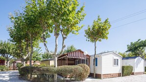 Une maison mobile dotée d’un porche, entourée d’arbres et bordée d’une allée en gravier.