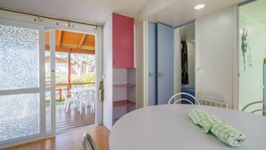 Une pièce avec une table blanche, une serviette verte, une porte en bois et une vue sur un espace extérieur aménagé avec des chaises.