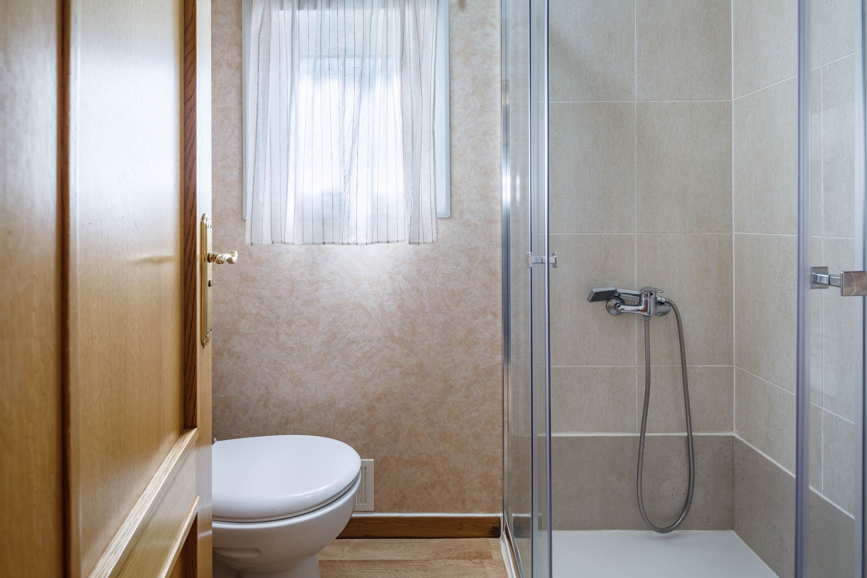 Ein Badezimmer mit Toilette, einer Dusche mit Glastür und einem Fenster mit Vorhang.