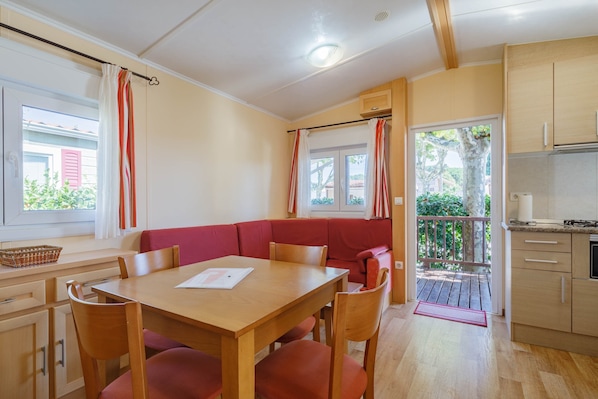 A room with a wooden dining table, red cushioned seating, a kitchen area, and a balcony with a railing.