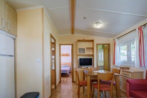 A compact room with a bed, a TV, a dining table, and a red sofa.